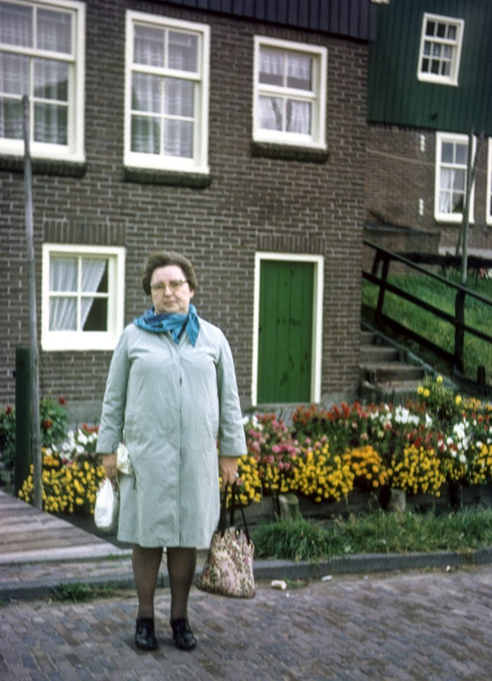 Free image of Woman posing for photograph in front of a home and flower bed.