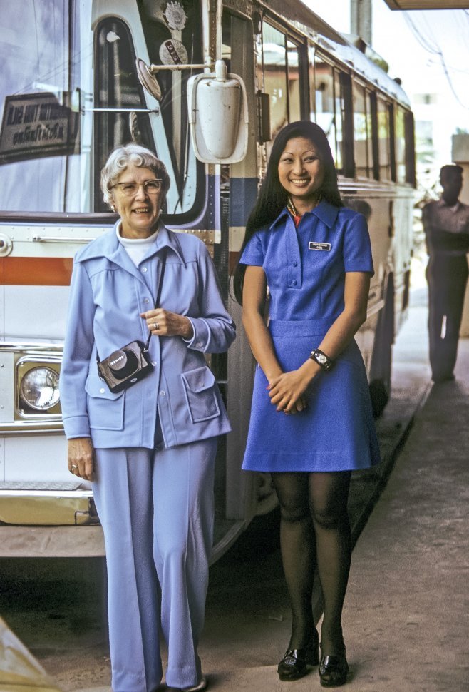 Free image of Tourist and her guide posing in blue suits in front of a tour bus, Thailand