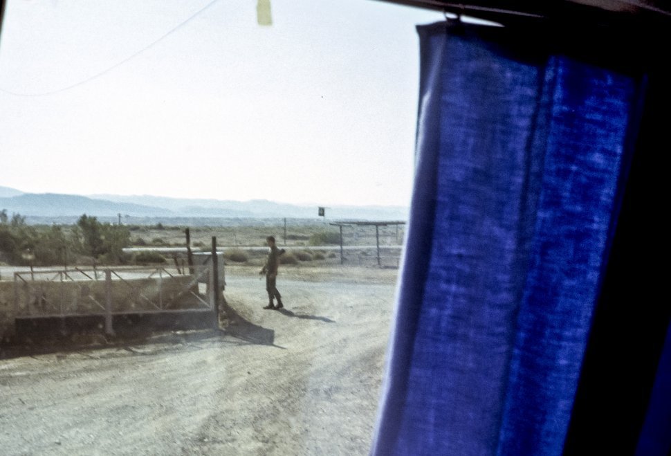 Free image of Image through a truck window of a guard walking along a dirt road.