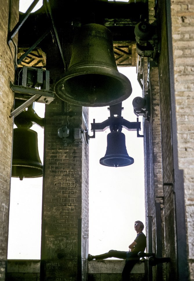 Free image of Man sitting beneath large church bells, Europe