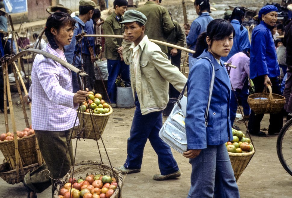 Free image of People carrying apples in baskets balanced on their shoulders marketplace, China