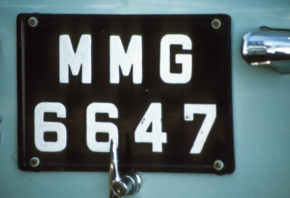 Free image of Close up of a black license plate and chrome handles on the back of a car.