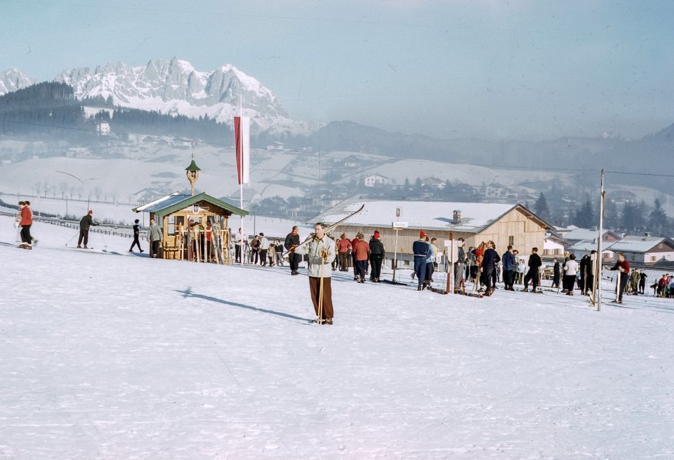 Free image of Woman posing in front of a crowd of skiers with her skis.