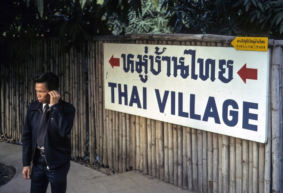 Free image of Man standing in front of a sign for a Thai village, circa 1974, Hong Kong, China