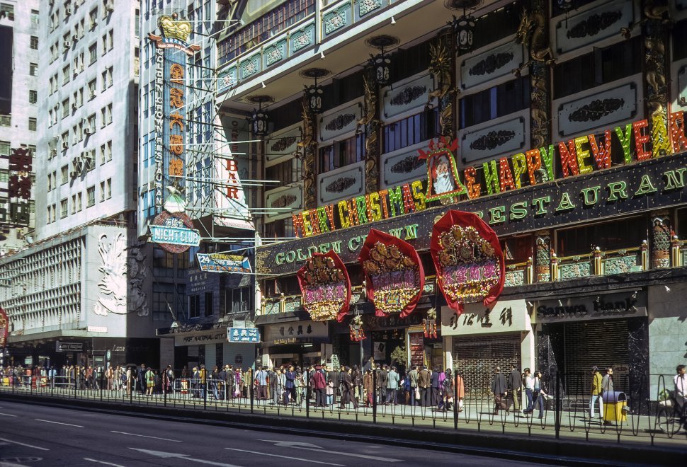 Free image of Stores, signs, and people lining a busy city street, circa 1974, Hong Kong, China