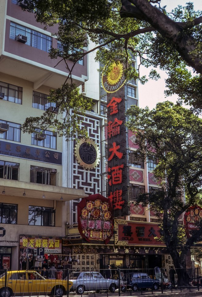 Free image of Stores, signs, and cars lining a street, circa 1974, Hong Kong, China