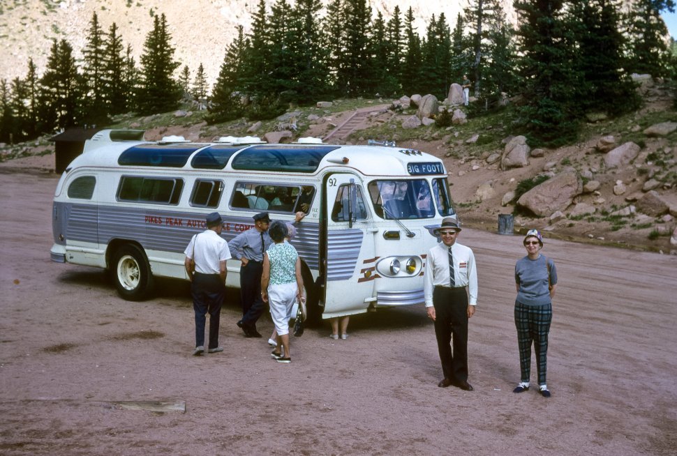 Free image of Group of tourists standing in front of a tour bus parked on the roadside, Pikes Peak, Colorado, USA