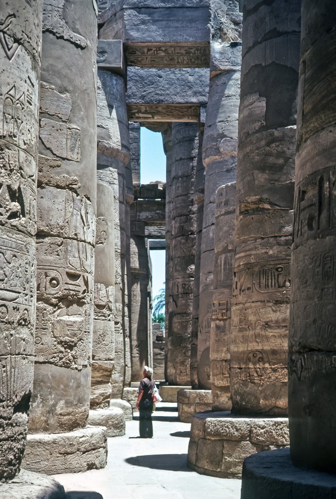 Free image of Tourist looking up at ancient Egyptian petroglyphs carved into a stone column, Egypt