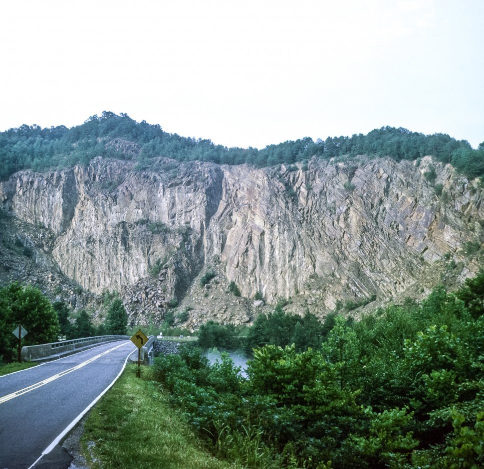 Free image of Image of a tall cliff face and tree line from roadside.