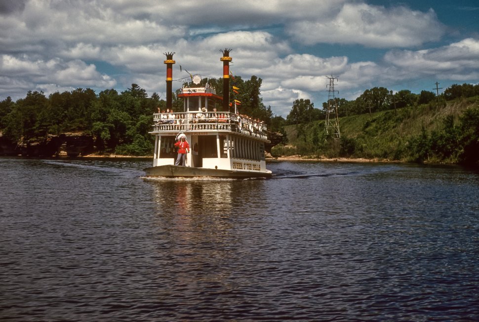 Free image of Themed tour boat sailing down a small river with a man in a Native American costume standing on the bow, Wisconsin Dells, Wisconsin, USA