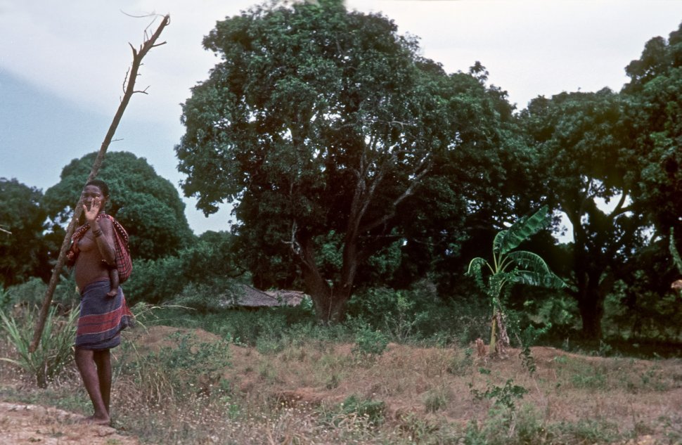 Free image of Tribal woman carrying her child on her back and waving at camera, Africa