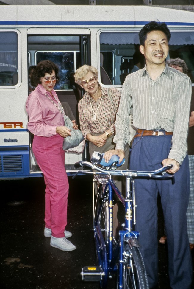 Free image of Women admiring a man s bicycle as he poses for a picture, China