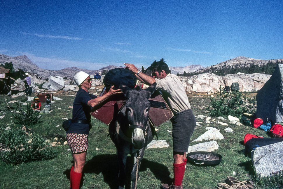 Free image of Two people loading camp site supplies onto a burro s back.